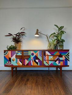 a colorful sideboard with potted plants sitting on it's sides and lights above