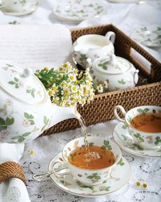 tea being poured into cups and saucers on a table with flowers in the background