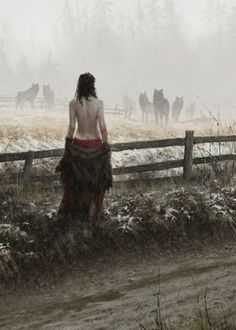 a woman standing in front of a fence with horses behind her on a foggy day