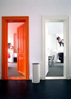 an orange door is in the middle of a room with white walls and black floors