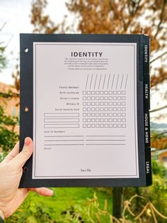 a person holding up a identity document in front of some trees and bushes with the word identity written on it