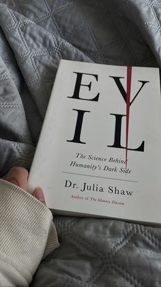 a person holding a book in their hand on top of a bed with white sheets