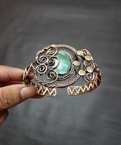 a hand holding a ring with a green stone in it's center and filigrees on the sides