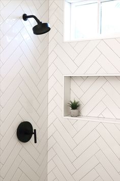 a white bathroom with black fixtures and herringbone tile on the walls, along with a potted plant