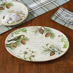 two plates with pine cones on them sitting on a wooden table next to napkins