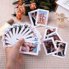 a hand holding four playing cards with pictures on them and flowers next to the deck