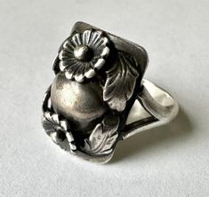 a silver ring with flowers on it sitting on a white surface, in front of a plain background