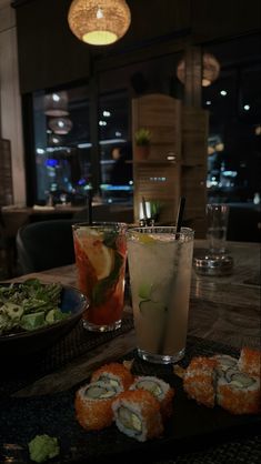 sushi and cocktails on a table in a restaurant at night with large windows