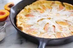 a close up of a pie in a pan on a table with peaches nearby