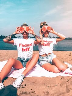 two women sitting on the beach holding slices of watermelon in front of their eyes