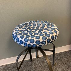 a blue and white patterned stool with black metal legs on carpeted floor next to gray wall