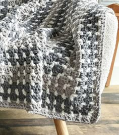 a gray and white crocheted blanket sitting on top of a wooden chair next to a window