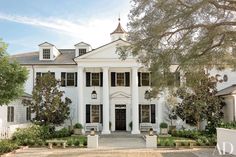 a large white house with black shutters on the front and side windows, surrounded by trees