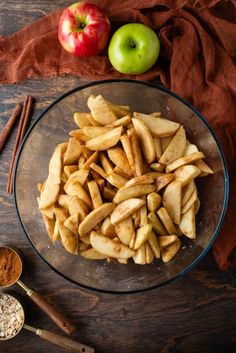 apple slices in a glass bowl next to cinnamon sticks and an apple on a wooden table