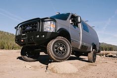 a large black truck parked on top of a dirt field next to trees and rocks