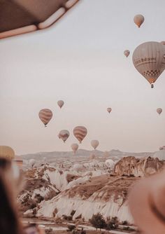 many hot air balloons are flying in the sky above some rocks and trees, while a woman is looking at them