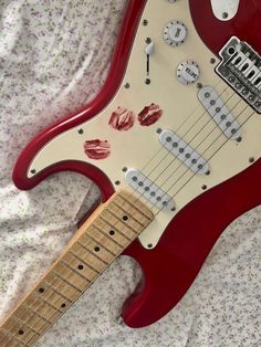 a red and white electric guitar laying on top of a bed next to a pillow