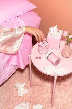 a pink table with tissues, hair dryer and other items on it next to a bed