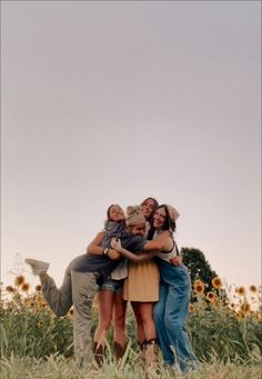 three girls and one boy are hugging in the middle of a field with sunflowers