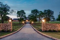 a gated driveway leading to a house with lights on at night in the evening