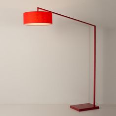 a red floor lamp sitting on top of a wooden table next to a white wall