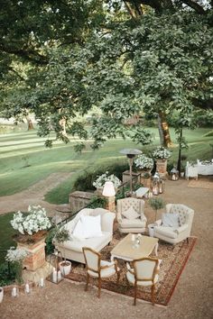 an outdoor seating area with chairs, tables and flowers on the ground in front of a large tree