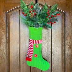 a green christmas stocking hanging on a wooden door with holly and berries in it