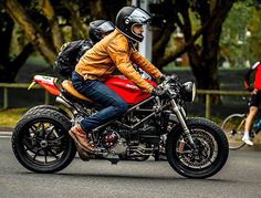 a man riding on the back of a red motorcycle down a street next to trees