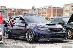 a blue subarunt is parked next to other cars in a parking lot with people looking at it