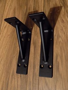 two black metal brackets sitting on top of a wooden floor