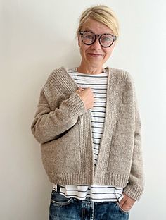 an older woman standing in front of a white wall wearing glasses and a cardigan