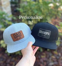 two hats with the words, personalize it and dad on them are held up in front of a garden