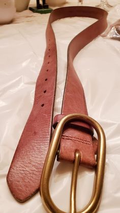 a pink belt with a gold buckle on it sitting on a white sheeted surface