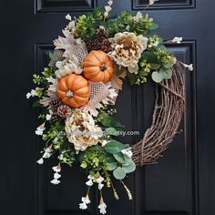 a wreath with pumpkins, flowers and greenery hangs on the front door's black door