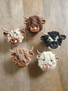 four cupcakes decorated to look like cows on a wooden table with brown and white icing