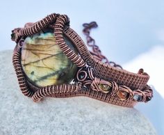 a wire wrapped bracelet with a leaf design on it sitting on top of a rock