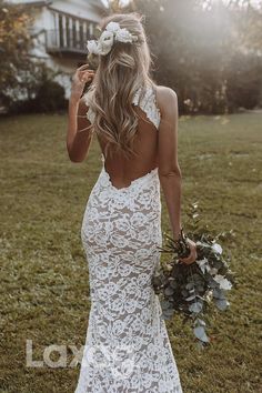 the back of a woman in a white wedding dress holding a bouquet and looking down