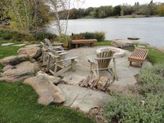 an outdoor fire pit surrounded by rocks and benches near a lake with trees in the background