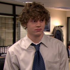 the young man is wearing a shirt and tie in an office setting with other people