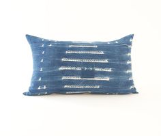 a blue and white pillow with lines on it, sitting against a white wall background