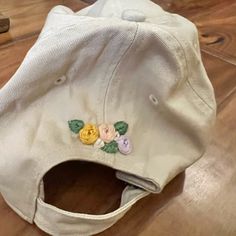 a white hat with embroidered flowers on it sitting on a wooden floor next to a pair of scissors