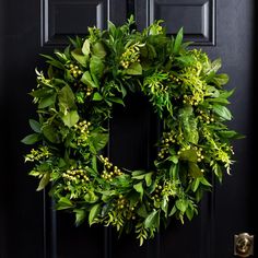 a green wreath on a black door with yellow flowers and leaves hanging from the front