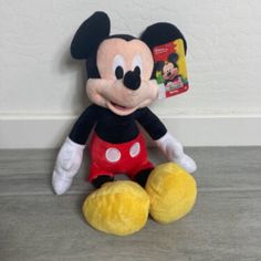 a mickey mouse stuffed animal sitting on top of a wooden floor next to a wall