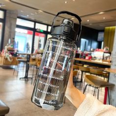 a person holding up a water bottle with words written on it in front of a restaurant