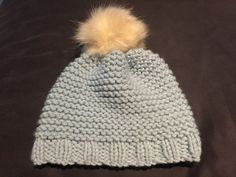 a white knitted hat with a yellow pom - pom sitting on top of a bed