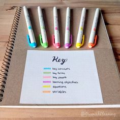 several pens are lined up on top of a notepad that has writing in it