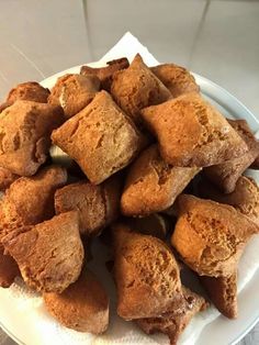 a white plate topped with lots of brown pastries on top of a wooden table