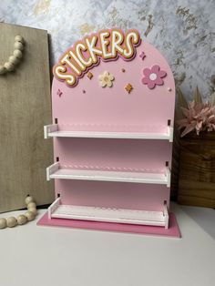 a pink display case with stickers on the top and flowers on the bottom, in front of a wallpapered background