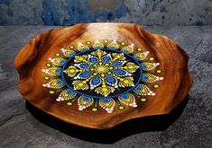 a wooden plate with an intricate design painted on the front and sides, sitting on a stone surface