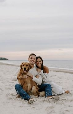 a man and woman sitting on the beach with their dog